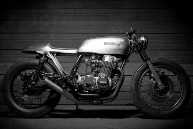 Black and white photo of a custom cafe racer motorcycle against a corrugated wall