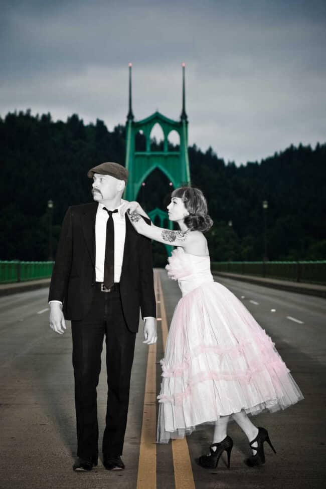 Selective color wedding-style photo of a couple on St. Johns Bridge in Portland, the man in a suit and the woman in a pink dress