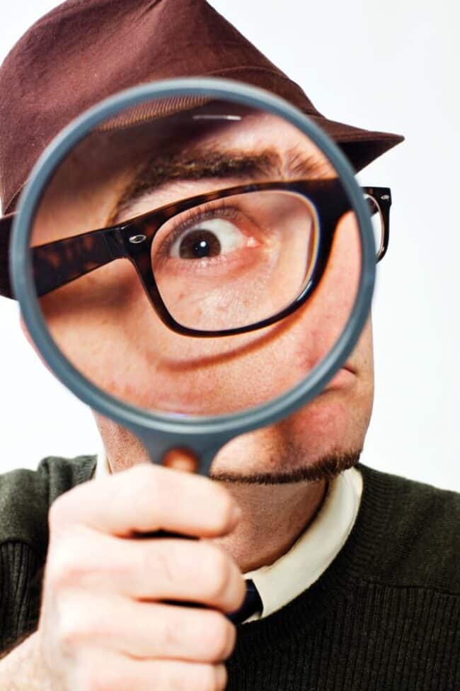 Playful portrait of a man in a flat cap looking through a magnifying glass