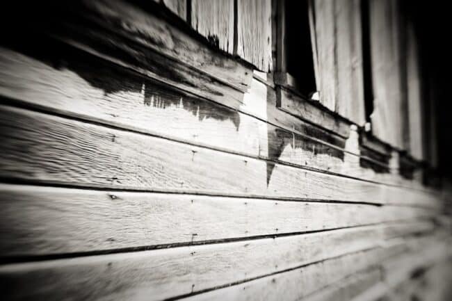 Black and white close-up of weathered wood siding and a window at an angle