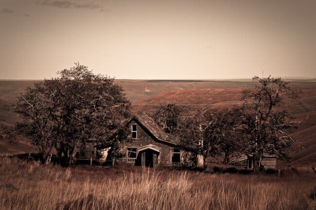Sepia-toned photo of an abandoned farmhouse in a rolling hills landscape