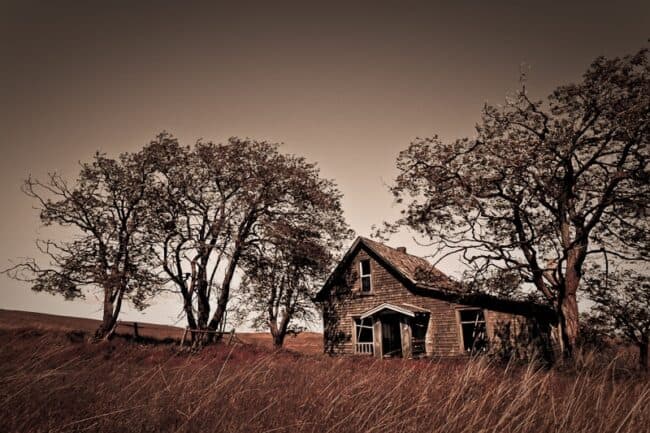 Sepia-toned photo of an abandoned wooden farmhouse among trees in a field