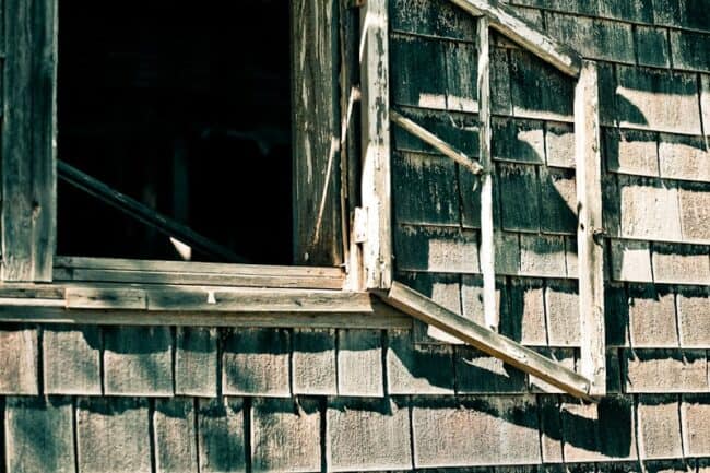 Broken window on a weathered wood-shingled building with dramatic shadows