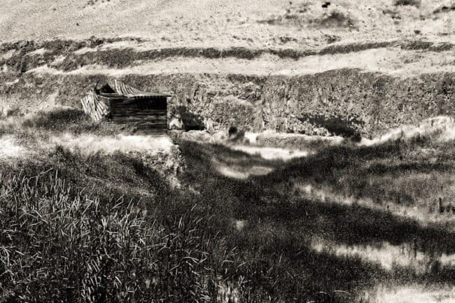 Black and white photo of a collapsed wooden structure on an eroded hillside