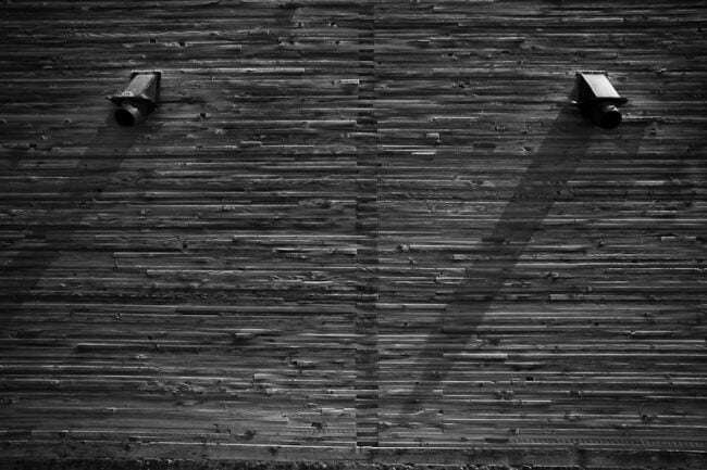 Black and white close-up of a corrugated metal wall with two vent fixtures casting long shadows