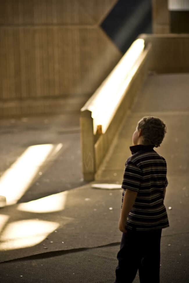 Young boy standing in shadow and light on a ramp, looking upward