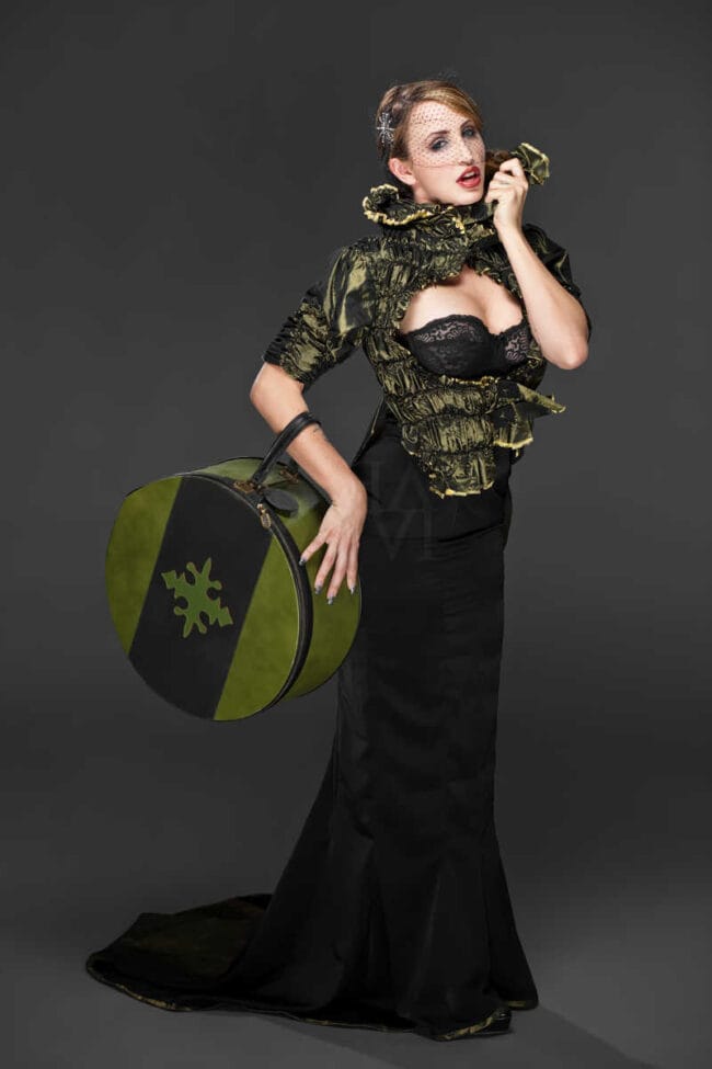 Woman in a black gown with a green ruffled bolero and veil holding a round patterned handbag