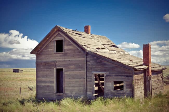 Abandoned old farmhouse with a brick chimney on the prairie under a blue sky