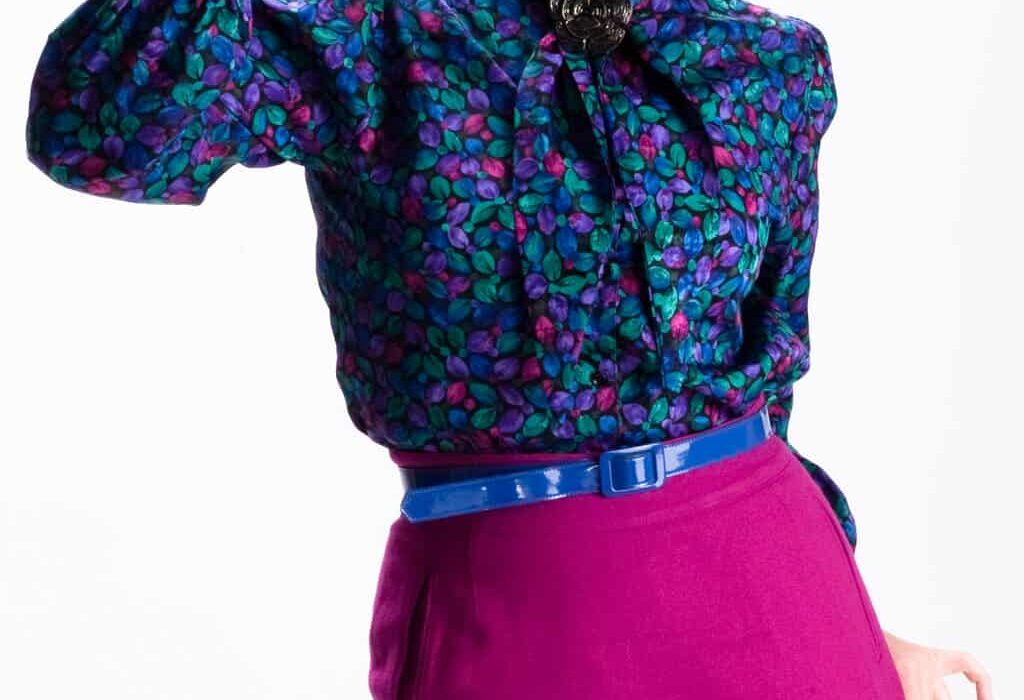 Woman in a colorful floral blouse and magenta skirt holding vintage binoculars in a studio portrait