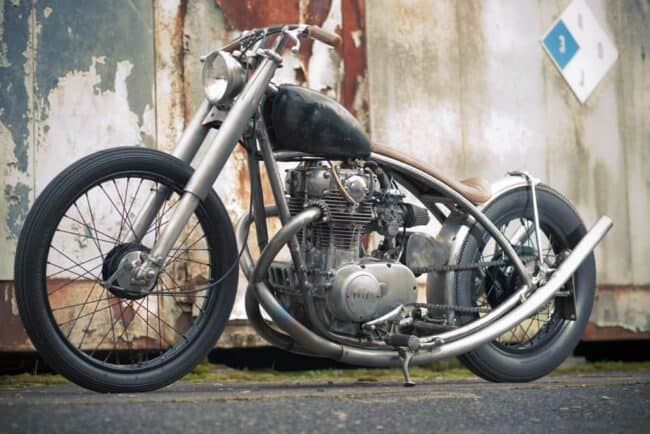 Custom bobber motorcycle parked against a rusted metal wall