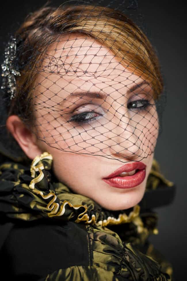 Close-up beauty portrait of a woman in a netted veil and gold-trimmed black dress