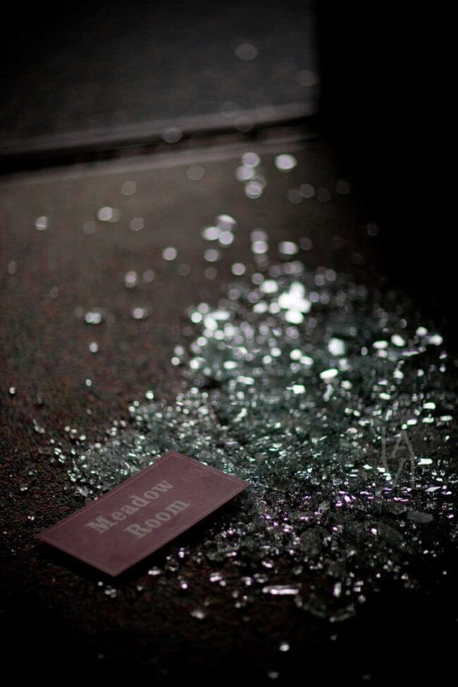 Close-up of shattered glass on the floor next to a 'Meadow Room' sign