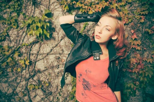 Woman in a leather jacket posing against an ivy-covered wall