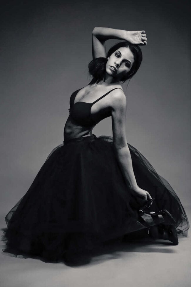 Black and white portrait of a woman in a black tulle gown holding her heels