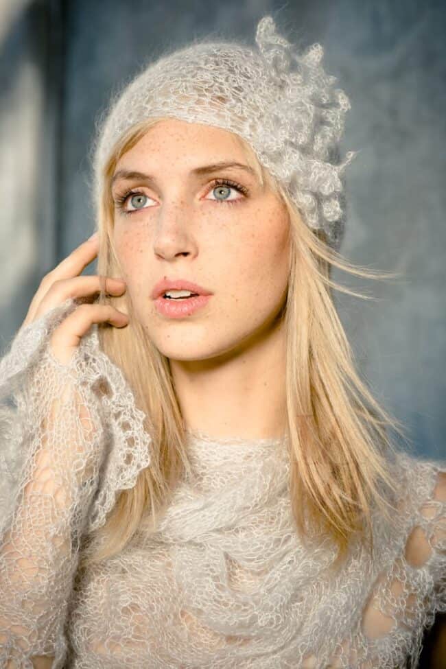 Portrait of a woman in a white lace hat and sweater holding her hand to her ear