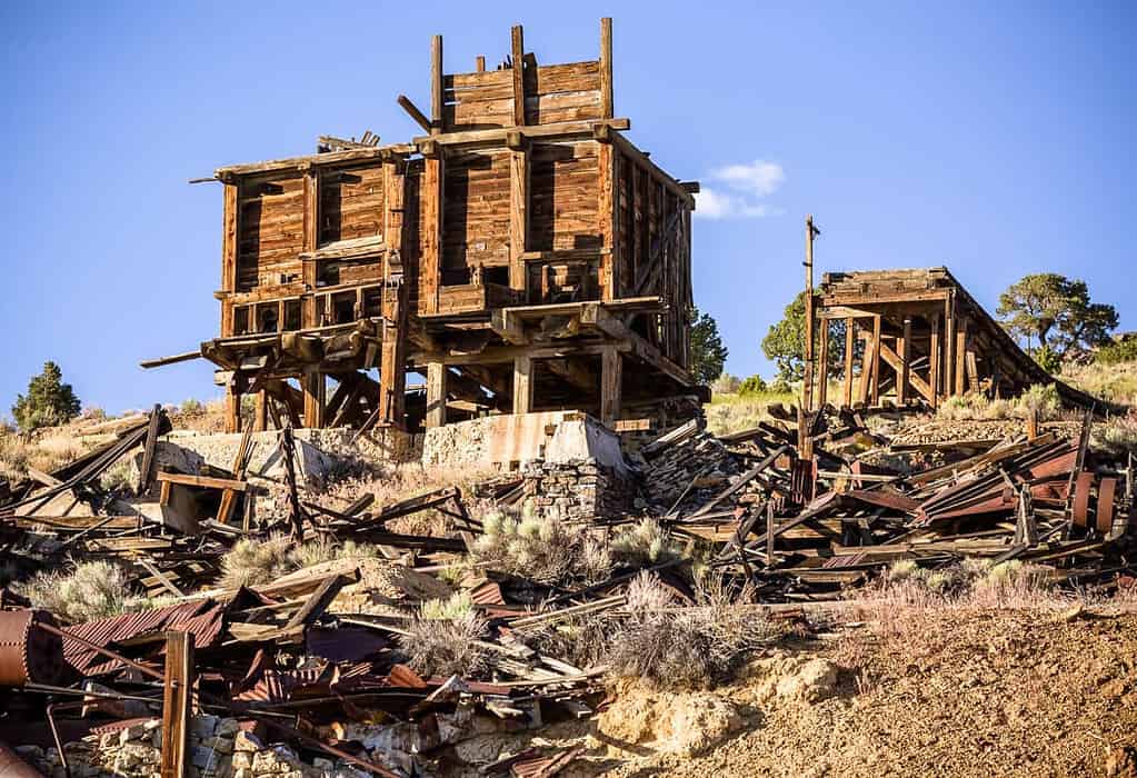 Ruins of a wooden mining structure with scattered debris on a hillside under a blue sky