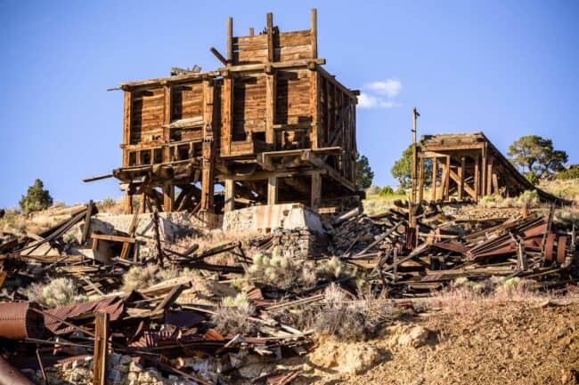Ruins of a wooden mining structure with scattered debris on a hillside under a blue sky