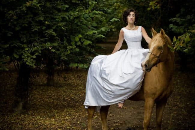 Woman in a white dress standing beside a horse in a forest