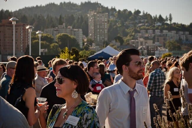Crowd of people mingling at an outdoor event with a city skyline in the background