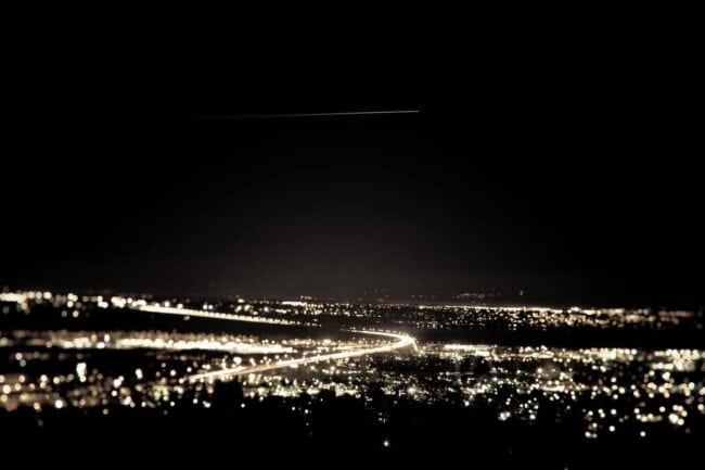 Aerial night view of city lights with a meteor streaking across the sky