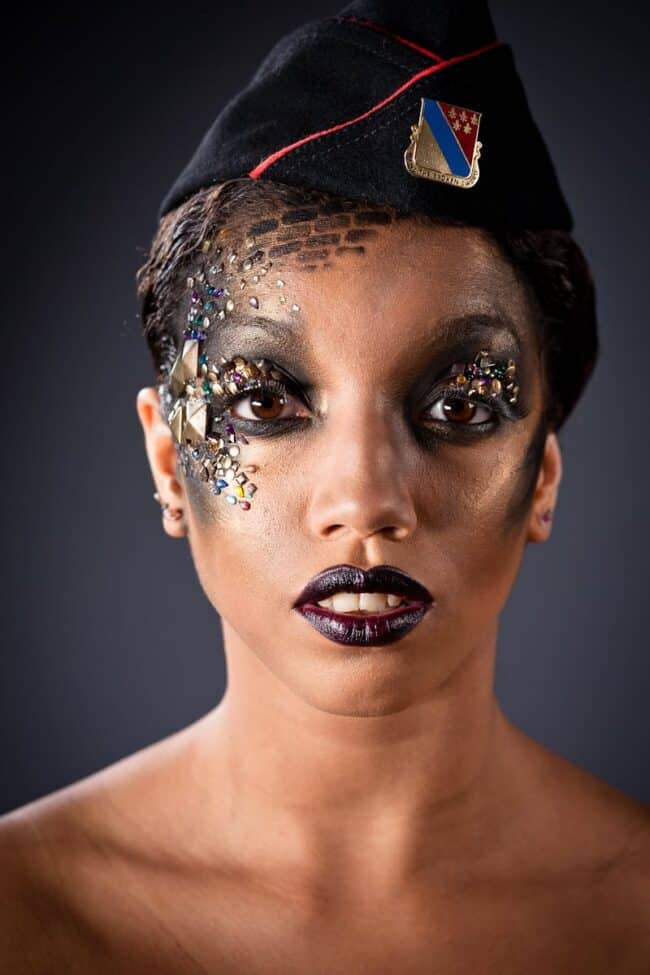 Avant-garde beauty portrait of a woman in a military garrison cap with rhinestones and dark makeup on her face