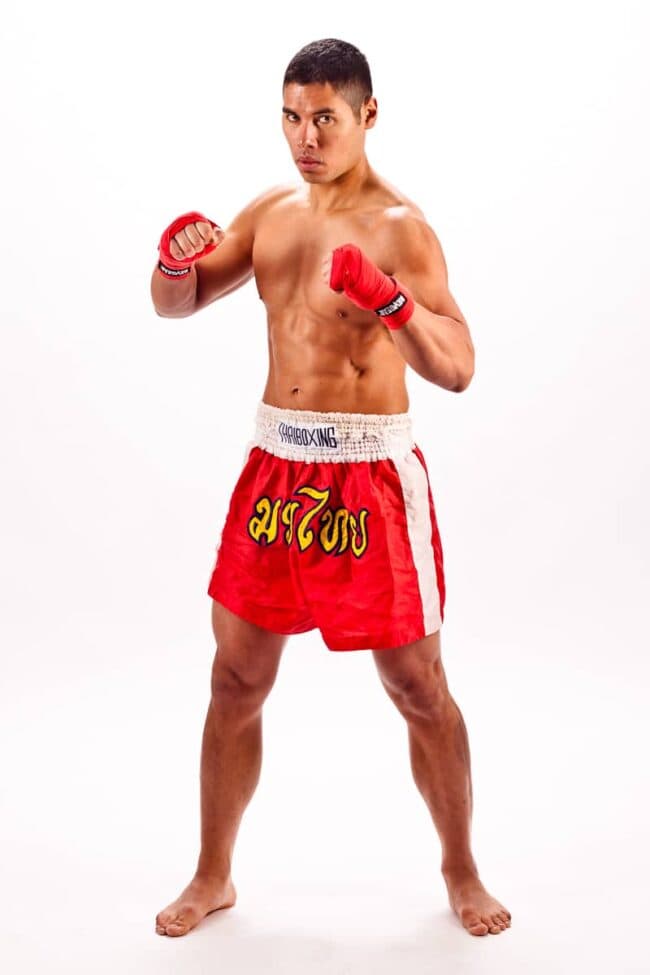 Shirtless man in red Muay Thai boxing shorts and gloves in a fighting stance, studio portrait