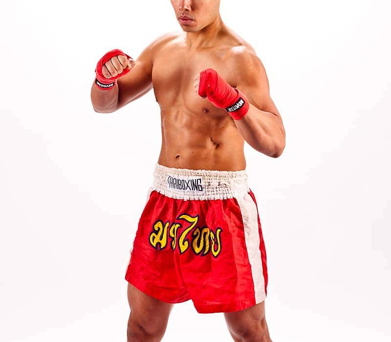 Shirtless man in red Muay Thai boxing shorts and gloves in a fighting stance, studio portrait