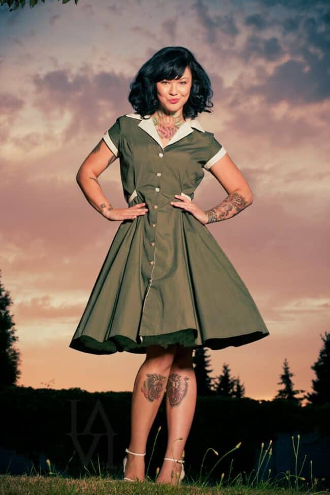 Portrait of a woman with tattoos and dark hair wearing a vintage green dress outdoors at dusk