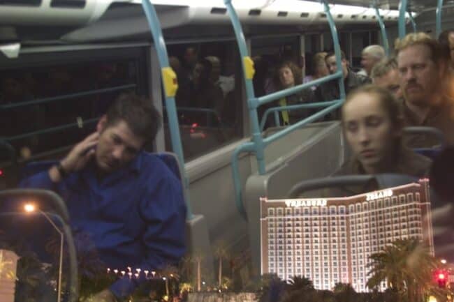 Tourists riding an open-top night bus tour with Treasure Island casino resort lit up in the background, Las Vegas