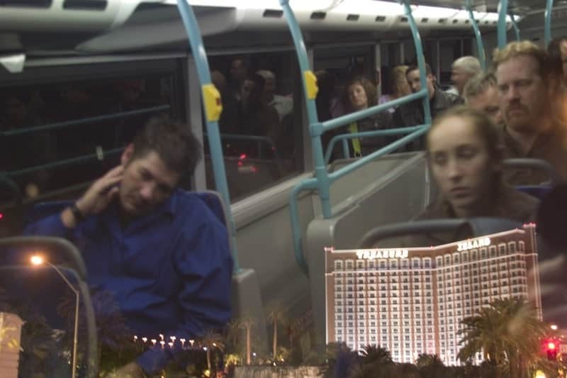 Tourists riding an open-top night bus tour with Treasure Island casino resort lit up in the background, Las Vegas