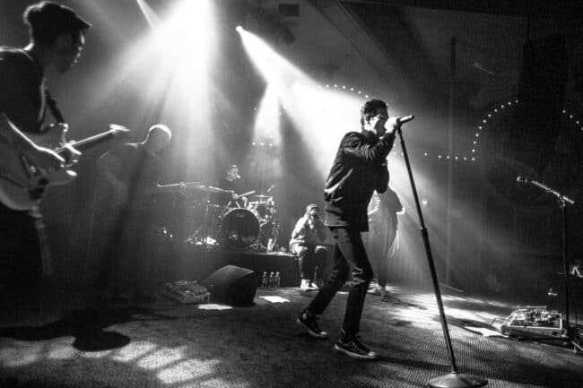 Black and white photo of a band performing on stage with dramatic spotlights