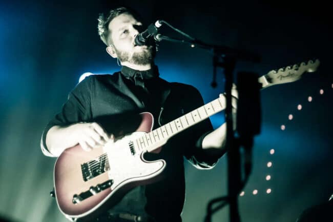 Musician singing and playing guitar on stage under blue stage lighting