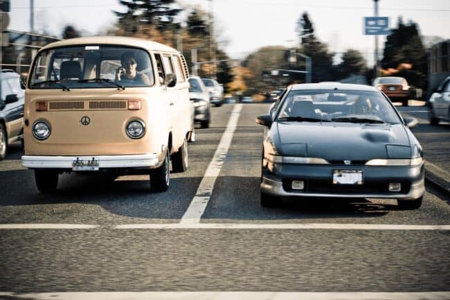 A vintage VW bus and a sports car stopped side by side at a traffic light
