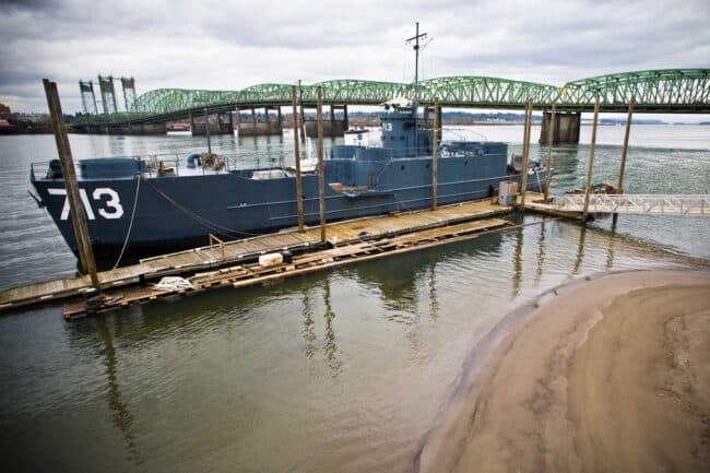 Decommissioned Navy vessel numbered 713 docked on a river near a green truss bridge