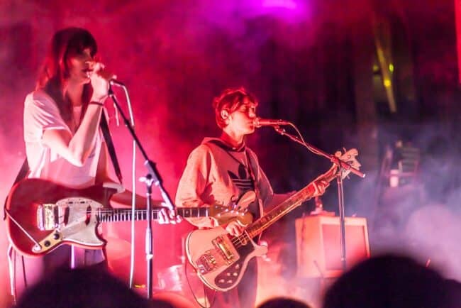 Two musicians performing on stage under red and purple concert lighting