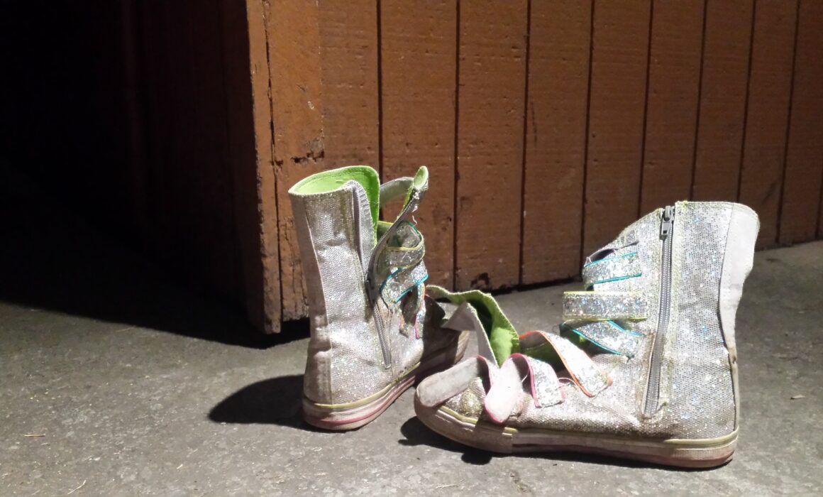 A pair of worn glittery children's boots on a concrete floor