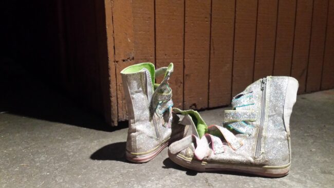 A pair of worn glittery children's boots on a concrete floor