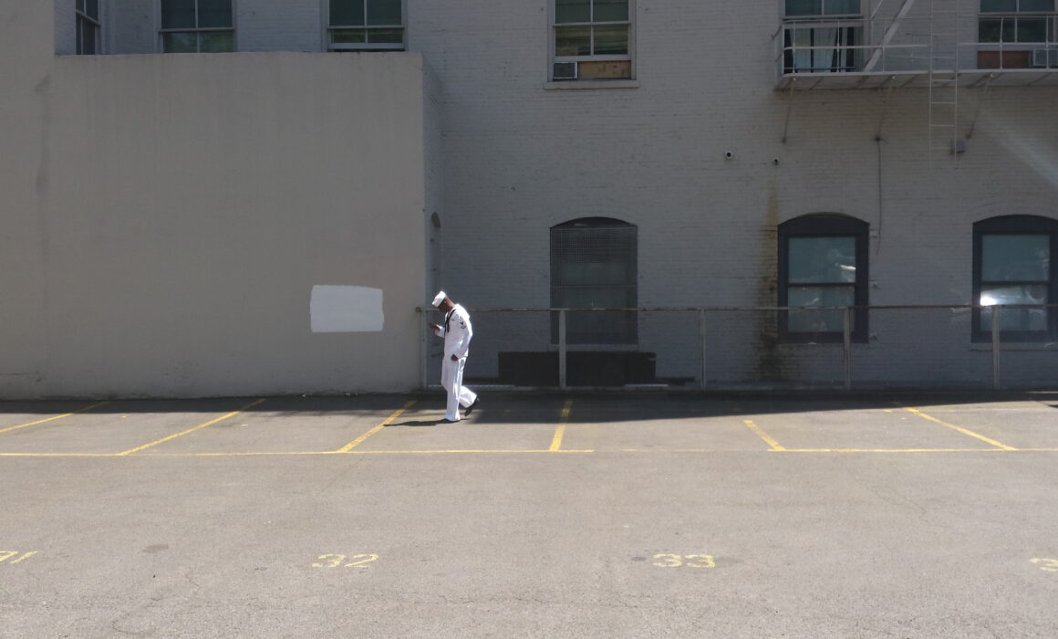 A person in a white uniform standing in an empty parking lot beside a brick building