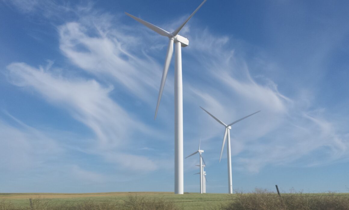Wind turbines against a blue sky with wispy clouds over a grassy field