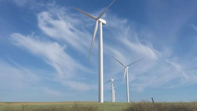 Wind turbines against a blue sky with wispy clouds over a grassy field