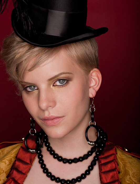 Portrait of a woman in a circus ringmaster costume with a top hat and black beaded jewelry