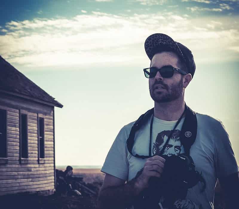 Photographer wearing a cap and sunglasses standing near an old prairie schoolhouse