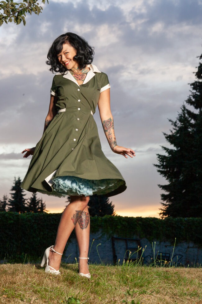 Fashion portrait of a woman in a green vintage dress twirling outdoors at sunset