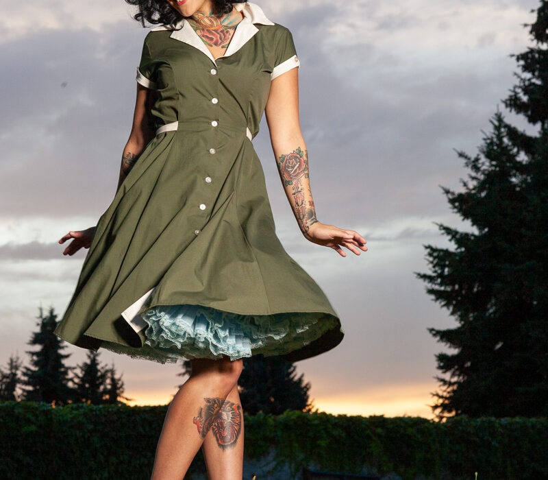 Fashion portrait of a woman in a green vintage dress twirling outdoors at sunset