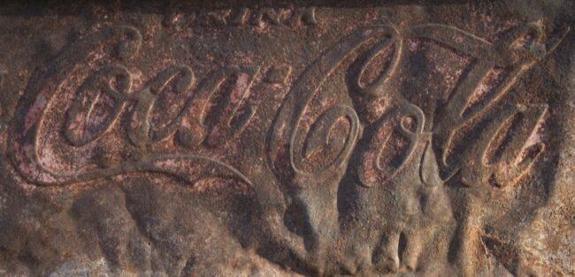 Close-up of a weathered vintage Coca-Cola sign embossed in rusted metal