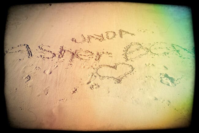 Names and a heart drawn in sand on a beach, retro film effect