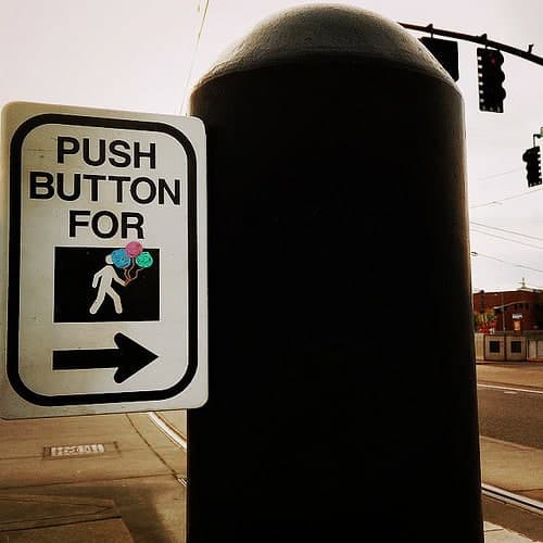 A 'Push Button For' pedestrian crossing sign mounted on a traffic signal pole