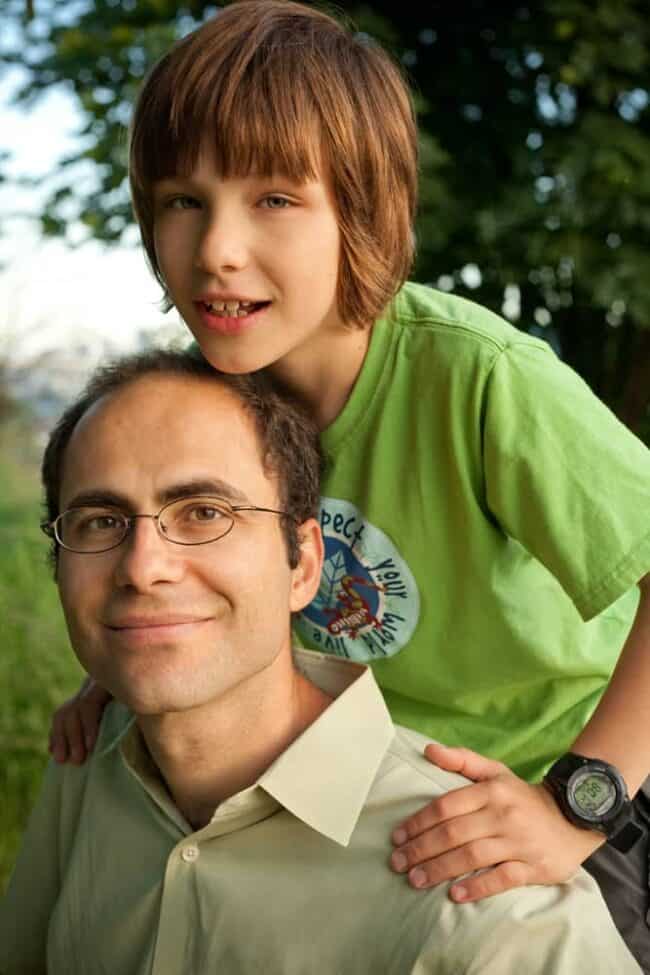 Portrait of a father and son smiling outdoors, the boy sitting on his father's shoulders