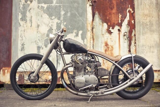 Custom bobber motorcycle parked in front of a rusted metal wall