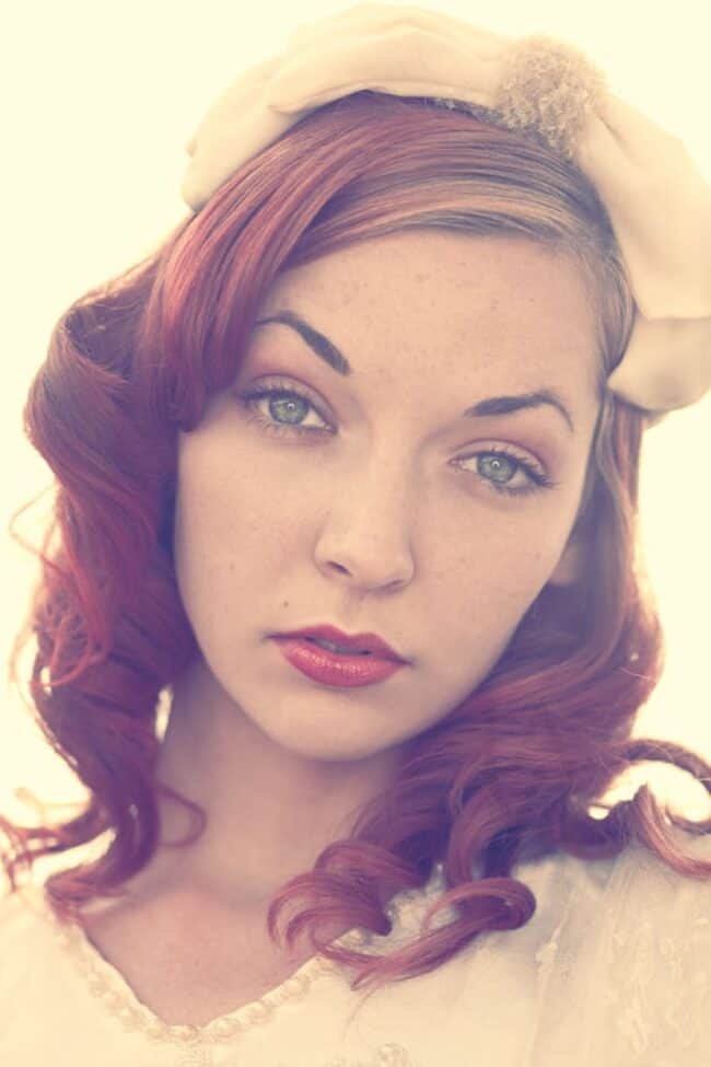 Portrait of a woman with red curled hair wearing a cream beret and lace top